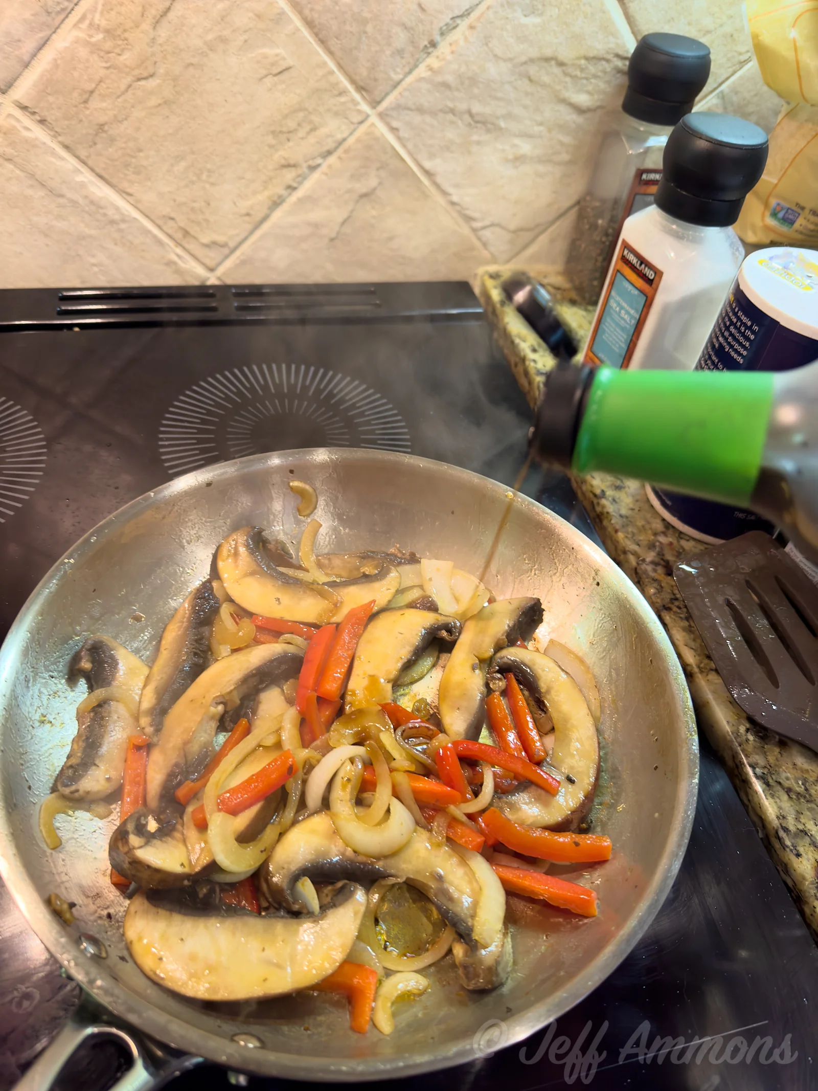 A hand pours a dark sauce from a bottle into a skillet of mushrooms, onion, and red bell pepper strips.