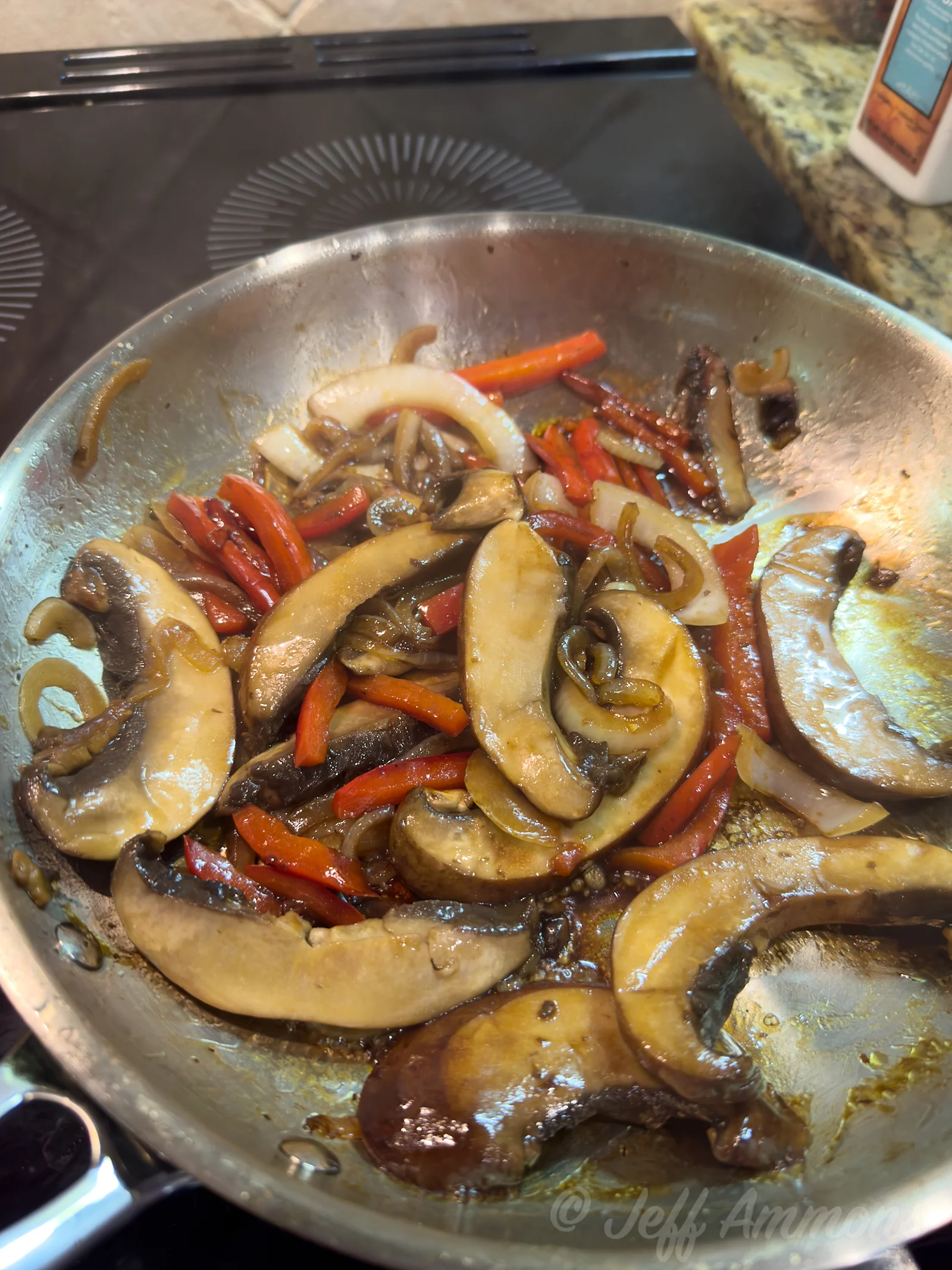 Cooked mushrooms, onions, and red bell peppers browned together in a skillet after the sauce has reduced.