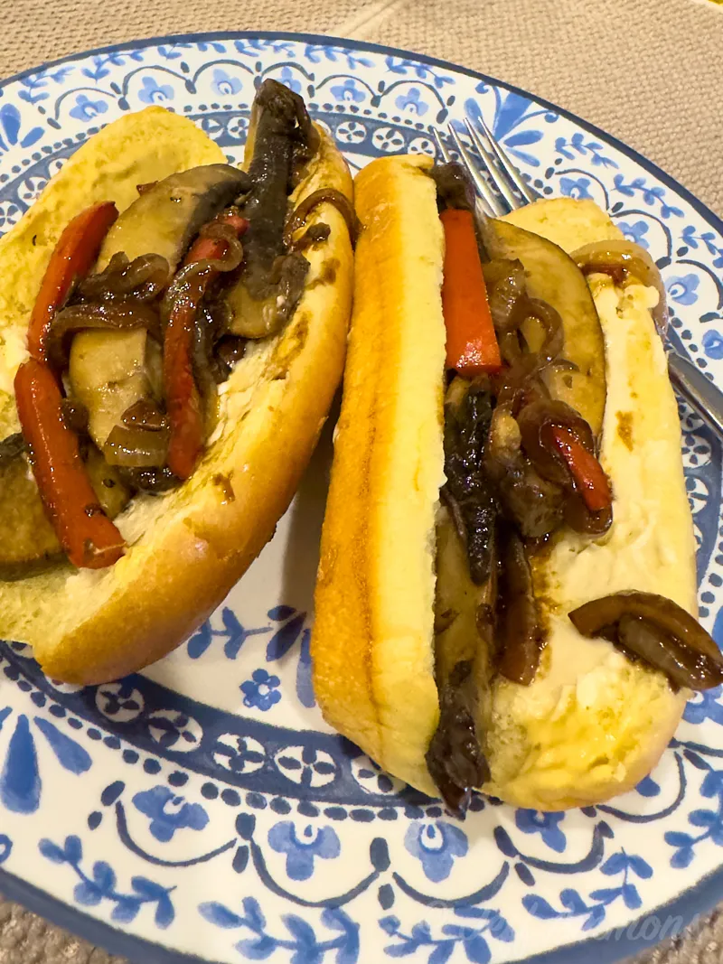 Two assembled sandwich buns filled with sauteed mushrooms, onions, and red bell peppers on a blue-and-white plate.
